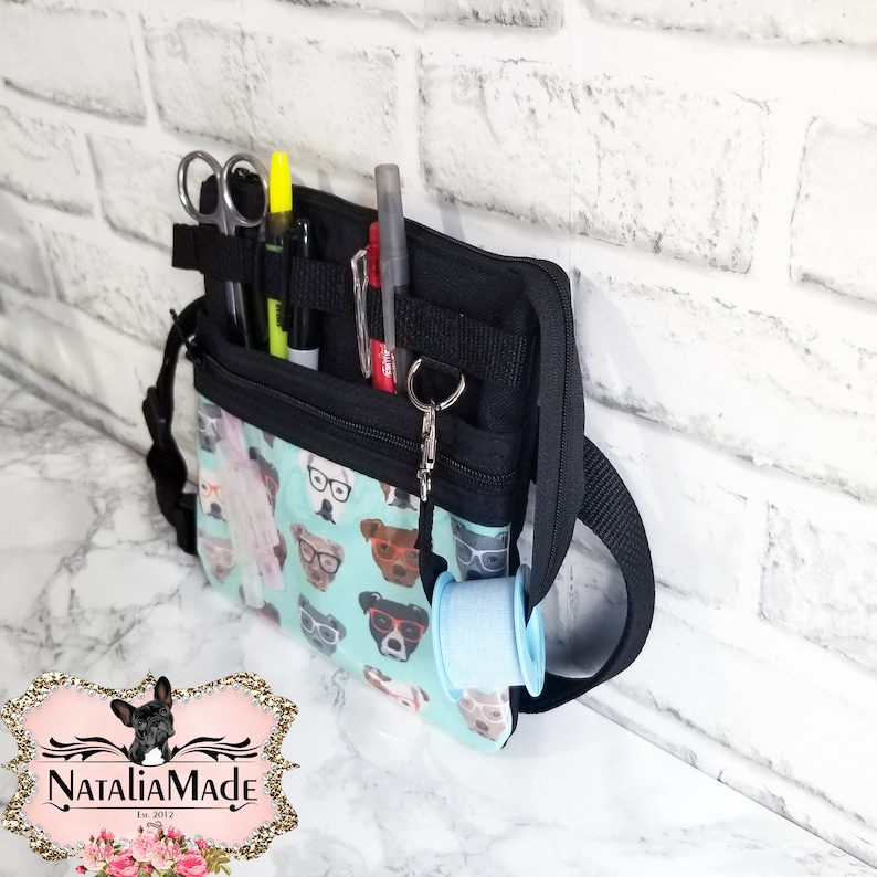 May include: A black and teal utility bag with a dog-themed pattern, featuring various tools and accessories. The bag has multiple compartments, including a section for scissors, pens, and a roll of tape. The bag is designed with a shoulder strap for easy carrying.