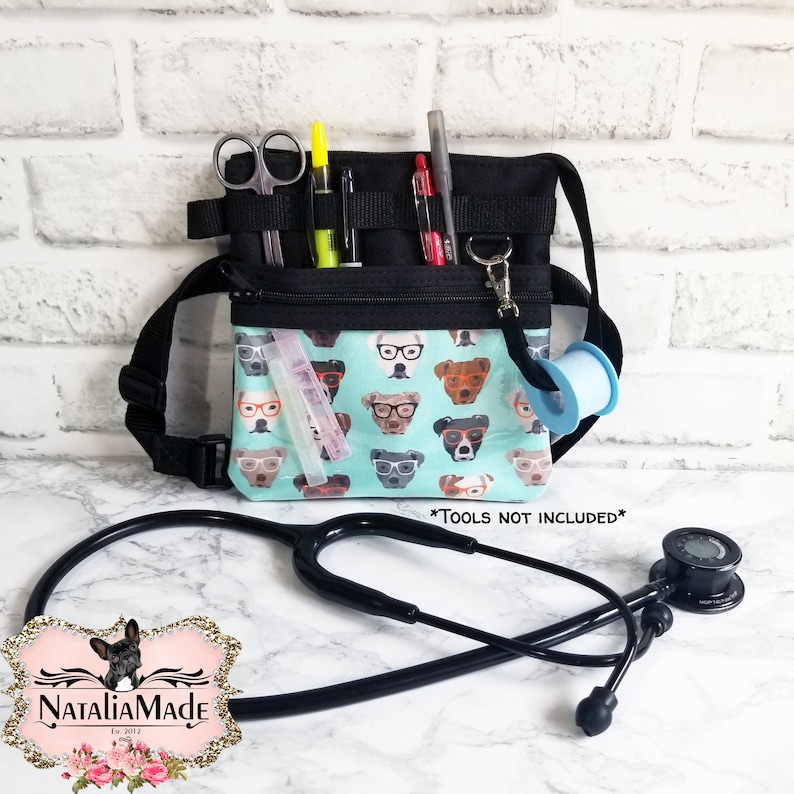May include: Black and teal medical fanny pack with a dog-in-glasses pattern. The pack has multiple pockets and loops for tools, including scissors, pens, and tape. A stethoscope is in the foreground. The text "*TOOLS NOT INCLUDED*" is visible.