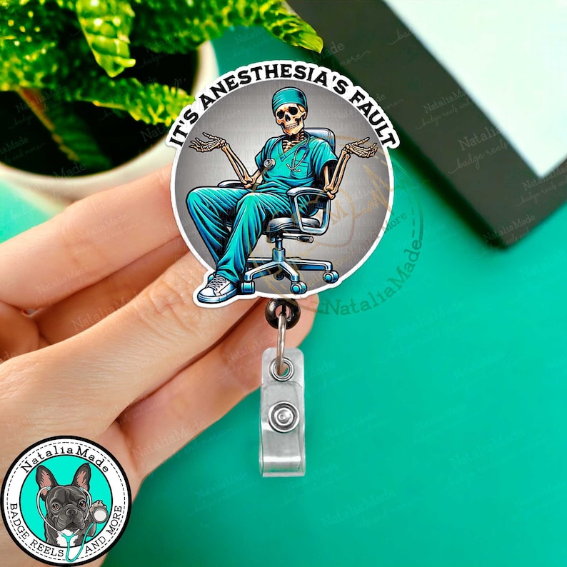 Op de afbeelding: Een ronde badgehouder met een skelet dat een blauwe operatiejas en een stethoscoop draagt. De badgehouder heeft de tekst "Het is de schuld van de anesthesie" in een witte cirkel op een grijze achtergrond.