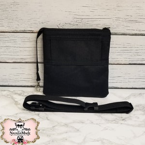 May include: A black crossbody bag with a zippered top and a small front pocket. The bag has a detachable strap and a silver-colored clasp. The bag is displayed on a white and gray marble surface.