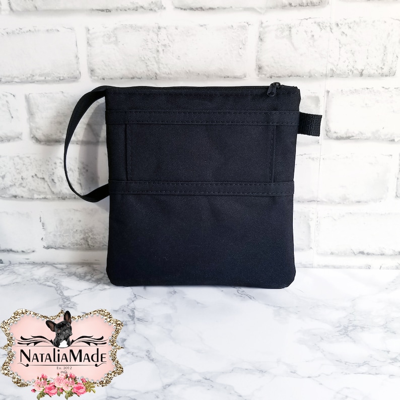 May include: A black crossbody bag with a zippered top and a small handle. The bag has two horizontal stitched lines across the front. The bag is sitting on a white and gray marble surface.