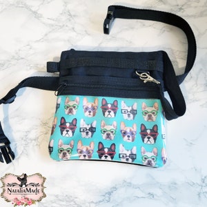 May include: Black and teal dog treat bag featuring a pattern of French Bulldogs wearing glasses. The bag has a black adjustable strap and a zipped pocket. A silver clasp is attached to the bag.