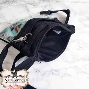 May include: Black fanny pack with a teal front pocket featuring a pattern of dog faces. The bag has a zippered main compartment and a silver-tone clasp. The brand name "NataliaMade" is visible in the bottom left corner.