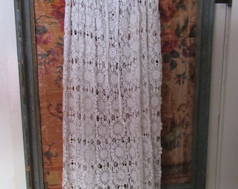 May include: White crochet skirt with a gathered waistband and a delicate lace pattern. The skirt is hanging on a hanger against a floral patterned background.