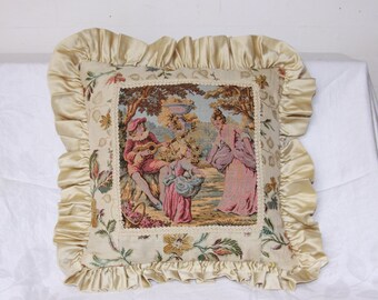 May include: A decorative pillow with a cream-colored background and a tapestry-style design featuring a couple playing music in a garden setting. The pillow has a ruffled border with a gold satin finish.