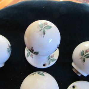 May include: Set of six white ceramic door knobs with a floral design. Each knob features a green stem with pink rosebuds and green leaves.
