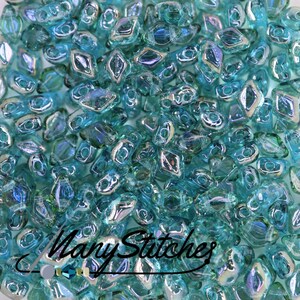 May include: A close-up of a pile of turquoise blue glass beads with an iridescent finish. The beads are shaped like small, elongated diamonds.