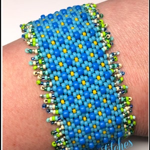 May include: A blue, yellow, and green beaded bracelet with the text "Many Stitches" on the bottom. Item #944-CF-Blue.