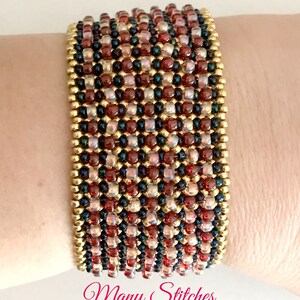 K&ouml;nnte beinhalten: Ein mehrfarbiges Perlenarmband mit goldenen Akzenten. Das Armband besteht aus kleinen, runden Perlen in Rot-, Braun- und Schwarzt&ouml;nen. Das Armband wird am Handgelenk einer Person getragen.