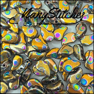 May include: A close-up of a pile of iridescent gold teardrop-shaped glass beads with a white background. The beads have a pattern of small, white dots on them.