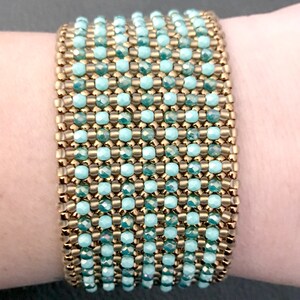 K&ouml;nnte beinhalten: Ein Armband mit abwechselnden Reihen aus goldenen und t&uuml;rkisfarbenen Perlen. Das Armband befindet sich an einem Handgelenk.