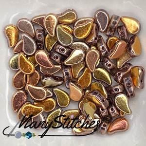 May include: A pile of small, teardrop-shaped glass beads in shades of gold, copper, and bronze. The beads have a metallic sheen and are perfect for jewelry making.