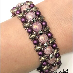 以下が含まれることがあります： 大理石模様の紫と金のビーズブレスレット。ブレスレットの名前は「セネガル」で、「Many Stitches」によって作られています。