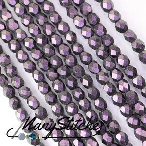 May include: A close-up of a strand of dark purple iridescent glass beads. The beads are faceted and have a metallic sheen.