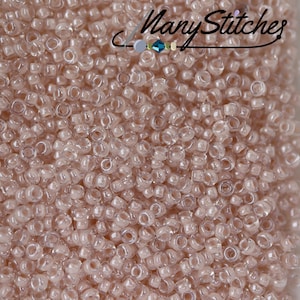 May include: A close-up image of a large quantity of small, translucent, light pink seed beads. The beads are arranged in a random pattern, creating a textured surface.