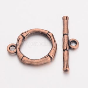 May include: A copper-toned metal toggle clasp with a round, bamboo-style ring and a straight bar with a loop at one end. The clasp is used for jewelry making.