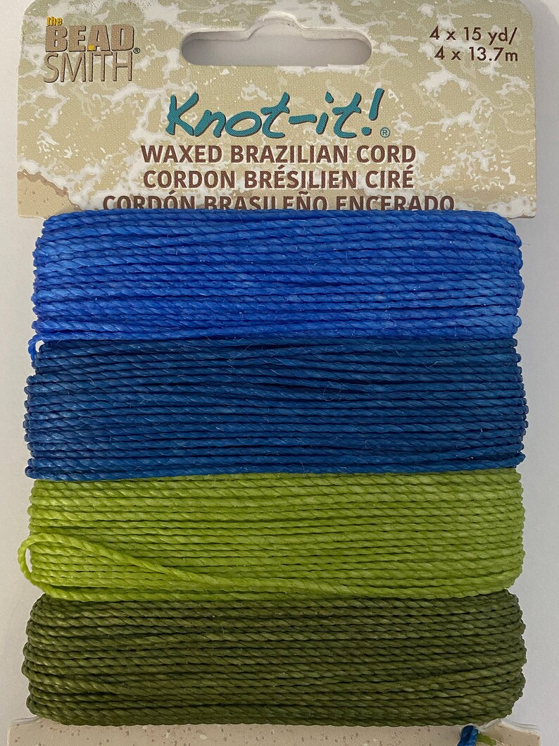 May include: Four spools of waxed Brazilian cord in blue, dark blue, green, and olive green. The cord is labeled "Knot-it! Waxed Brazilian Cord, Cordon Br&eacute;silien Cir&eacute;, Cord&oacute;n Brasile&ntilde;o Encerado".