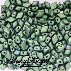 Puede incluir: Primer plano de un montón de pequeñas cuentas de vidrio verde facetadas. Las cuentas tienen un brillo metálico y tienen forma de diamantes.