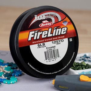 May include: A spool of "FireLine" microfused braided bead thread by The Beadsmith. The label indicates 6LB, 125YD, and "Crystal" color. The spool is black with a red and orange label. The thread is used for jewelry making.