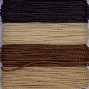 May include: A spool of waxed thread with four different colors: black, cream, brown, and cream. The thread is wound tightly on the spool.