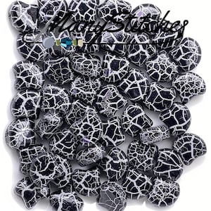 May include: A close-up of a group of black and white crackle glass beads. The beads are shaped like a rounded rectangle and have a white crackle design on a black background.
