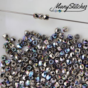 May include: A pile of iridescent silver-toned faceted glass beads. The beads are small and have a multi-colored sheen.