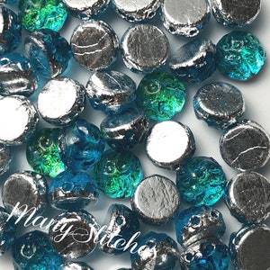 May include: A collection of glass beads in shades of silver, teal, and blue. The beads have a textured, faceted design. The text "Mary Stitches" is visible in the image, along with the item number "908-AQ".