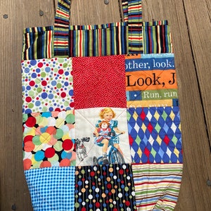 May include: A quilted tote bag with a patchwork design featuring various colorful patterns, including polka dots, stripes, and a girl riding a bicycle. The bag has a black, green, and yellow striped handle and the text "other, look. Look, J. Run, run." is printed on the front.
