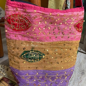 May include: A multi-colored fabric handbag with gold sequins and embroidery. The bag has a pink, brown, and purple design with a black zipper closure.