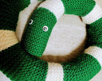 May include: A knitted snake toy in green and white. The snake has googly eyes and is coiled. The body is green with white bands. The toy is made of yarn and is likely a children's toy or decorative item.