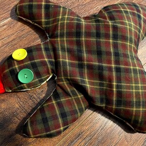 May include: A plaid fabric turkey with a red felt head and yellow and green buttons for eyes.