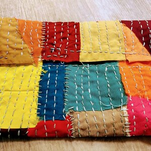 May include: A patchwork quilt made of different colored fabric squares, sewn together with white thread. The quilt is made of yellow, orange, red, blue, and brown fabric.