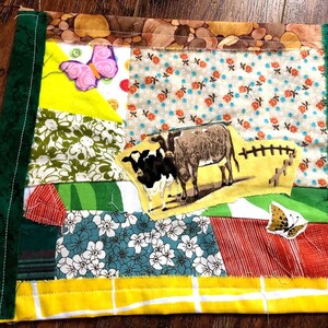 May include: A patchwork quilt with a green border, featuring a yellow, green, and white floral pattern, a red and white striped pattern, a blue and white floral pattern, and a yellow and brown cow pattern. The quilt also features two butterflies, one pink and one brown.