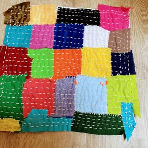 May include: A colorful patchwork quilt made of various fabrics sewn together in a grid pattern. The quilt is made of different colors, including red, green, blue, yellow, and orange. The quilt is stitched with white thread.