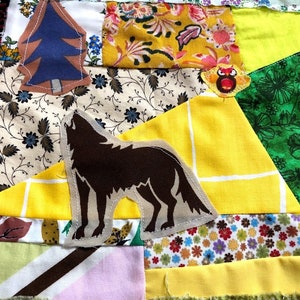 Puede incluir: Una colcha de retazos con una silueta de lobo marrón, un pino azul, un pájaro amarillo y varios patrones florales en tonos de amarillo, verde y blanco.