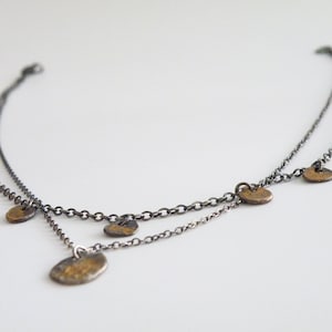 Puede incluir: Un collar de cadena de plata con varios colgantes pequeños, redondos y de color dorado. El collar está formado por dos cadenas.