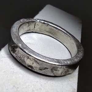 May include: A silver ring with a hammered texture. The ring is thick and has a wide band.