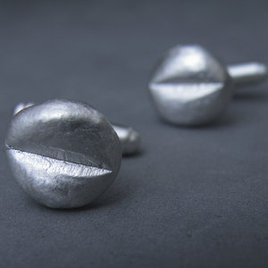 May include: A pair of silver cufflinks shaped like a screw head. The cufflinks have a smooth, polished finish.