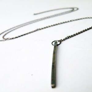 May include: A silver chain necklace with a long, thin, silver pendant.