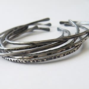 May include: A set of five silver bangles with a hammered finish. The bangles are stacked on top of each other, creating a layered look.