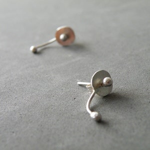 May include: A pair of silver earrings with a small round disc and a curved stem ending in a small ball.