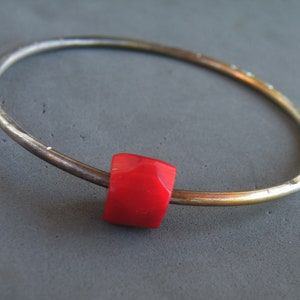 May include: A silver bangle bracelet with a bright red, faceted gemstone bead.