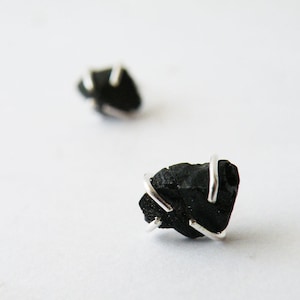 May include: A pair of black stone earrings with silver wire accents. The stones are irregularly shaped and have a rough texture.