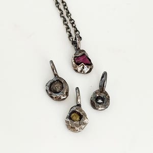 Peut inclure: Quatre pendentifs en argent avec des pierres de différentes couleurs à l'intérieur. Les pendentifs sont sur un fond blanc.