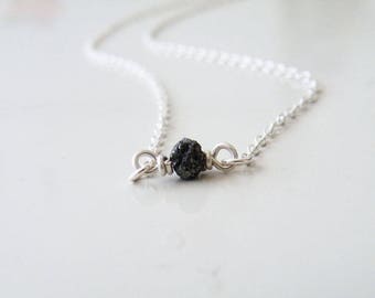 May include: A delicate silver chain necklace with a single black diamond pendant.