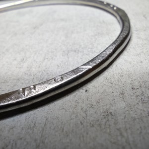 Peut inclure: Un bracelet en métal argenté avec une surface texturée et un petit cercle gravé dans le métal.