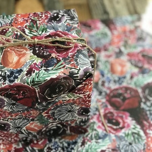 Peut inclure: Une bo&icirc;te cadeau envelopp&eacute;e de papier &agrave; motifs floraux avec un motif aquarelle de fleurs roses, rouges et vertes. La bo&icirc;te est attach&eacute;e avec de la ficelle.