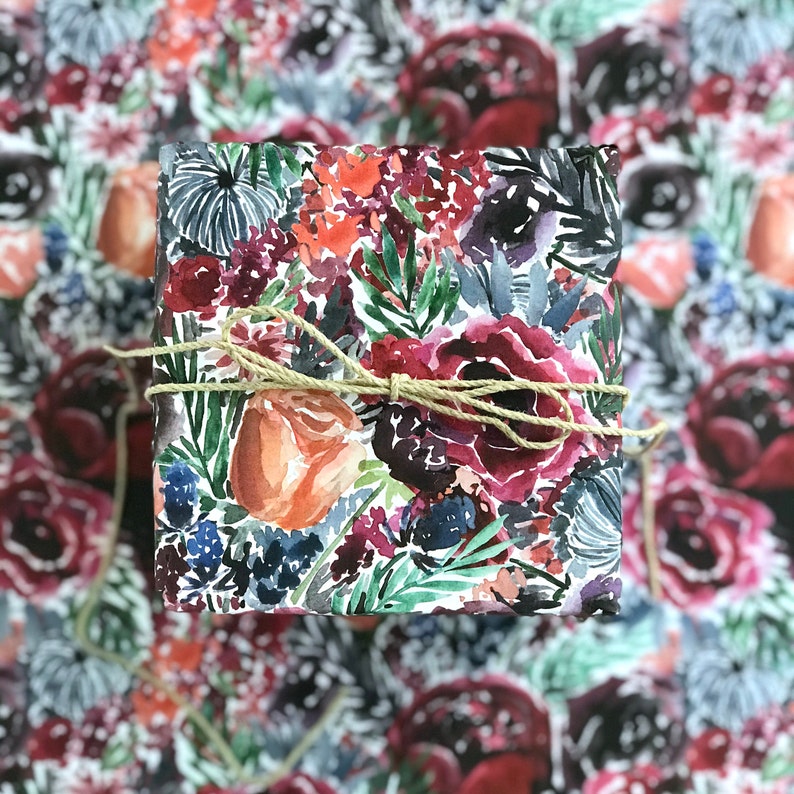 Peut inclure: Une bo&icirc;te cadeau carr&eacute;e envelopp&eacute;e de papier blanc &agrave; motif floral. Le papier pr&eacute;sente des illustrations &agrave; l'aquarelle de fleurs, de feuilles et de baies rouges, roses, orange et bleues. La bo&icirc;te est attach&eacute;e avec un n&oelig;ud en ficelle naturelle.