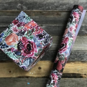 Peut inclure: Une bo&icirc;te cadeau envelopp&eacute;e de papier &agrave; motifs floraux. Le papier pr&eacute;sente un motif aquarelle de fleurs roses, rouges et orange avec des feuilles vertes sur un fond blanc.