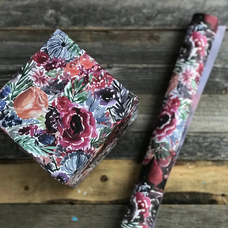 Peut inclure: Une bo&icirc;te cadeau envelopp&eacute;e de papier &agrave; motifs floraux. Le papier pr&eacute;sente un motif aquarelle de fleurs roses, rouges et orange avec des feuilles vertes sur un fond blanc.